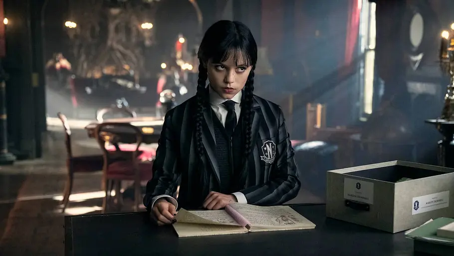Wednesday Addams sitzt am Schreibtisch und liest Akten eines Kriminalfalls.