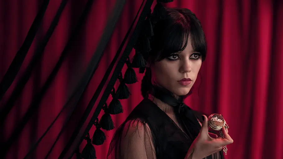„Wednesday“ Staffel 3 Wednesday Addams steht vor einem dunkelroten Vorhang und hält eine Taschenuhr in der Hand.