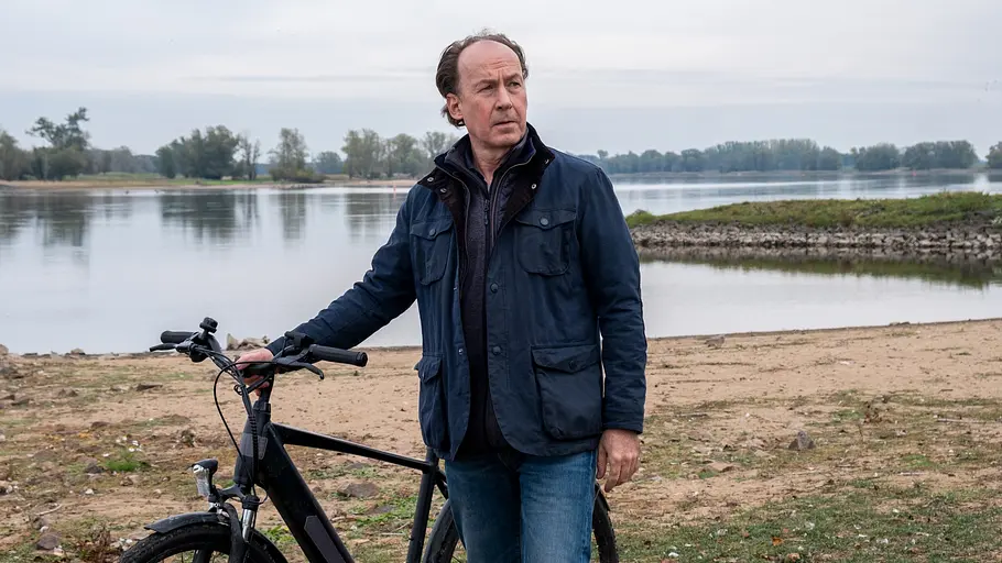 Wendland - Stiller und das große Schweigen Jakob Stiller (Ulrich Noethen) steht mit seinem Fahrrad am Ufer.