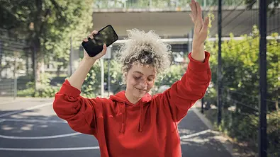 Eine junge Frau mit Kopfhörern im Ohr und Smartphone in der Hand tanzt draußen. - Foto: © Vodafone