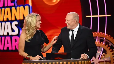 Barbara Schöneberger und Stefan Raab führen durch die neue Show „Wer weiß wie wann was war?“. - Foto: RTL / Raab Entertainment / Willi Weber / Hintergrund KI-generiert