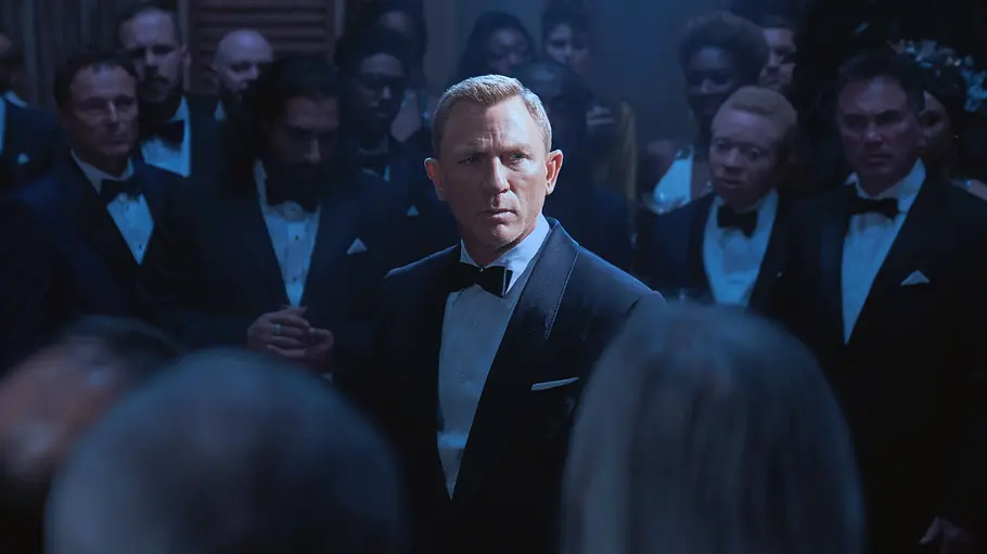 No Time to Die James Bond im Anzug wird von vielen weiteren Anzugträgern umringt.