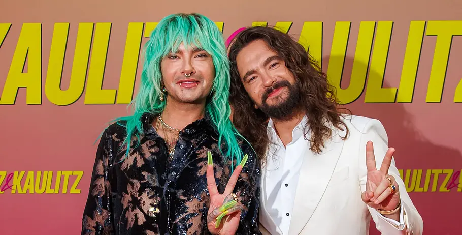 Bill und Tom Kaulitz bei der Premiere von Kaulitz und Kaulitz von Netflix, lächeln in die Kamera und machen mit der Hand ein Peace-Zeichen.