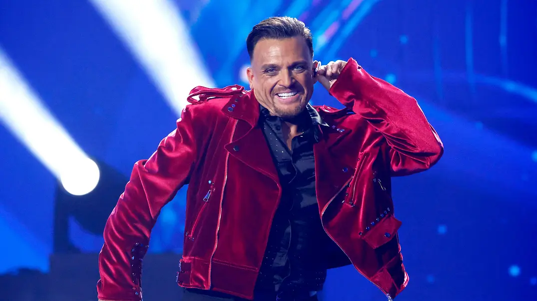 Menowin in roter Jacke mit Mikrofon. - Foto: IMAGO / Panama Pictures Menowin in roter Jacke mit Mikrofon. - Foto: IMAGO / Panama Pictures