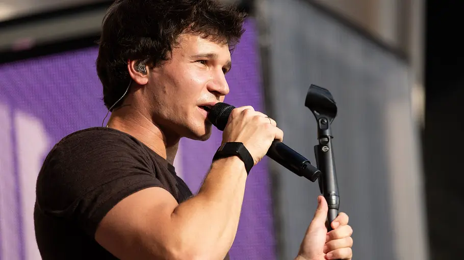 Wincent Weiss hält auf einer Bühne ein Mikrofon an den Mund und greift mit der anderen Hand den Mikrofonständer.