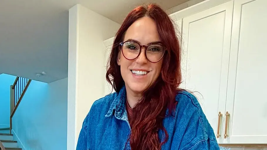 Liz Tomforde Eine Frau mit langen roten Haaren und Brille steht in einer modernen Küche und lächelt in die Kamera.