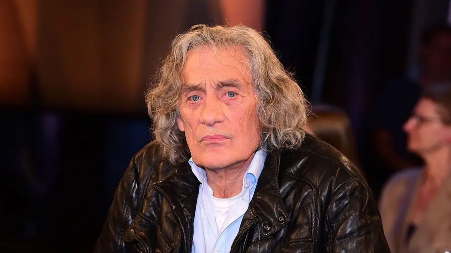 Winfried Glatzeder Winfried Glatzeder trägt eine schwarze Lederjacke und ein hellblaues Hemd. Er guckt bedrückt in die Kamera.