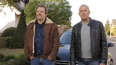 Briefe aus dem Jenseits? Winni Karls (Ronald Kukulies, l. ) und Ingo Thiel (Heino Ferch) stehen vor einem Auto und blicken in die Ferne. - Foto: ZDF/Tom Trambow Briefe aus dem Jenseits? Winni Karls (Ronald Kukulies, l. ) und Ingo Thiel (Heino Ferch) stehen vor einem Auto und blicken in die Ferne. - Foto: ZDF/Tom Trambow