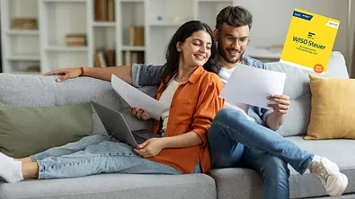 Ein junges Paar sitzt mit Laptop und Zetteln auf der Couch. Sie machen Ihre Steuer. - Foto: istock/Olena Miroshnichenko/PR