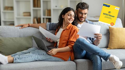 Ein junges Paar sitzt mit Laptop und Zetteln auf der Couch. Sie machen Ihre Steuer. - Foto: istock/Olena Miroshnichenko/PR