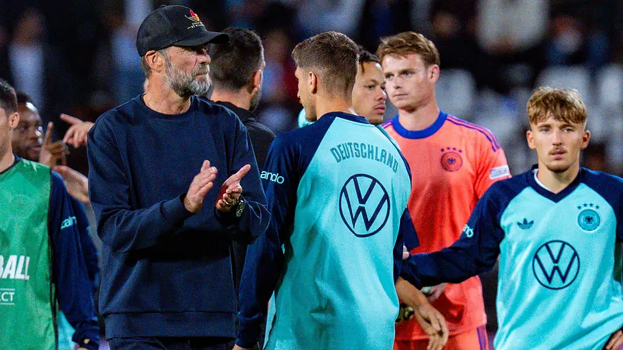 WM 2030 Übertragung Jürgen Klopp steht mit schwarzer Kappe zwischen Spielern der deutschen Fußballnationalmannschaft und klatscht.
