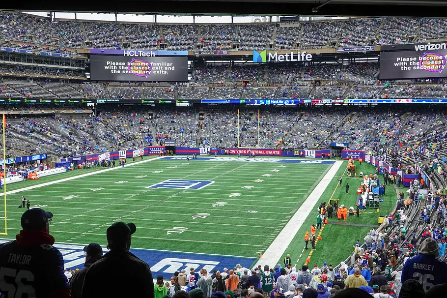 Metlife Stadium New York Blick ins MetLife Stadium während eines Footballspiels: Das Spielfeld mit den Markierungen der New York Giants ist von zahlreichen Zuschauern in den Rängen umgeben, große Videotafeln hängen über den Tribünen, und Fans verfolgen die Partie von ihren Plätzen aus.