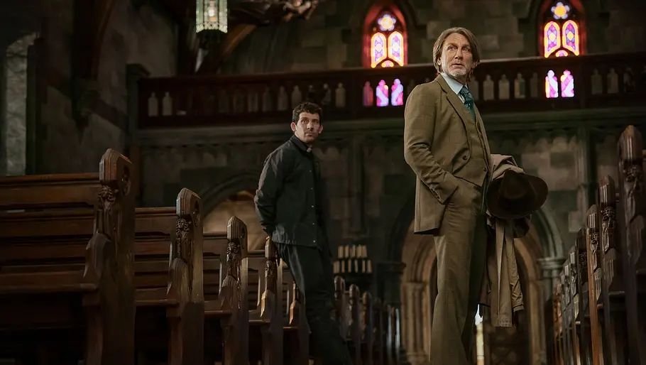 Benoit und Paster Jud stehen in der Kirche und schauen beide nach vorne.