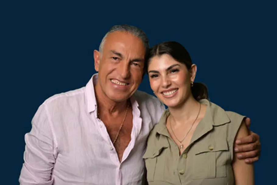 Yeliz Koc und ihr Vater Savas stehen lächelnd vor dunkelblauem Hintergrund. Er hat den Arm um ihre Schulter gelegt.