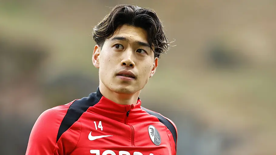 Fußballspieler im roten Trainingsoberteil des SC Freiburg blickt während des Aufwärmens aufmerksam zur Seite. Im Hintergrund ist das Stadion unscharf zu erkennen.