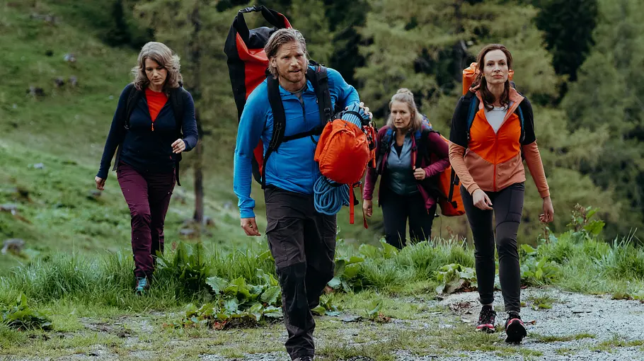 Yvonne Kern (Dagny Dewath, r.), Sandra Piazelli (Eva-Maria Grein von Friedl, l.) und Emilie (Stefanie von Poser, 2. v. r.) Die Bergretter: Ein letzter Augenblick (1): Auf eine Bergpfad: Rücksäcke tragend laufen Sandra Piazelli (Eva-Maria Grein von Friedl), Yvonne Kern (Dagmar Dewath), Emilie (Stefanie von Poser) und Markus (Sebastian Ströbel) mit Abstand zueinander eine Steigung hinauf. Die Stimmung zwischen ihnen wirkt angespannt.