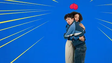 Maximilian Mundt und Naomi Simmonds umarmen sich vor blauem Hintergrund mit gelben Strahlen. Über ihnen hängt ein rotes Herz in Form eines Hodensacks. - Foto: ZDF/Adrian Gross Maximilian Mundt und Naomi Simmonds umarmen sich vor blauem Hintergrund mit gelben Strahlen. Über ihnen hängt ein rotes Herz in Form eines Hodensacks. - Foto: ZDF/Adrian Gross