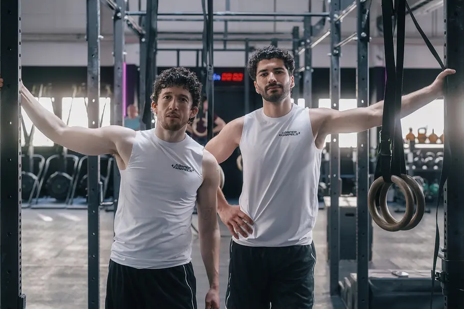 ZDF-Serie „Ballz“ mit Maximilian Mundt. Maximilian Mundt und Mohamed Kanj Khamis in weißen, ärmellosen Shirts stehen in einem Fitnessstudio an einem Trainingsgestell mit Turnringen.