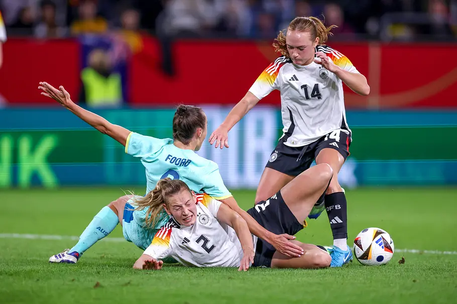 Caitlin Foord und Sarai Linder liegen nach einem Zweikampf am Boden. Lisanne Gräwe steht daneben, der Ball liegt rechts.