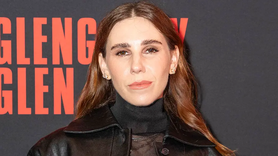 Zosia Mamet Zosia Mamet trägt eine schwarze Lederjacke über einem transparenten Oberteil vor einer dunklen Wand mit roter Schrift.