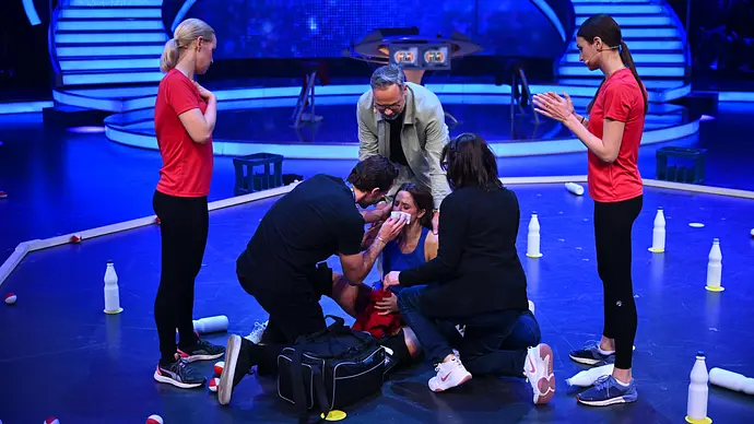 Vanessa Mai sitzt auf dem Boden und wird während von zwei Pfleger:innen versorgt. - Foto: ProSieben / Willi Weber